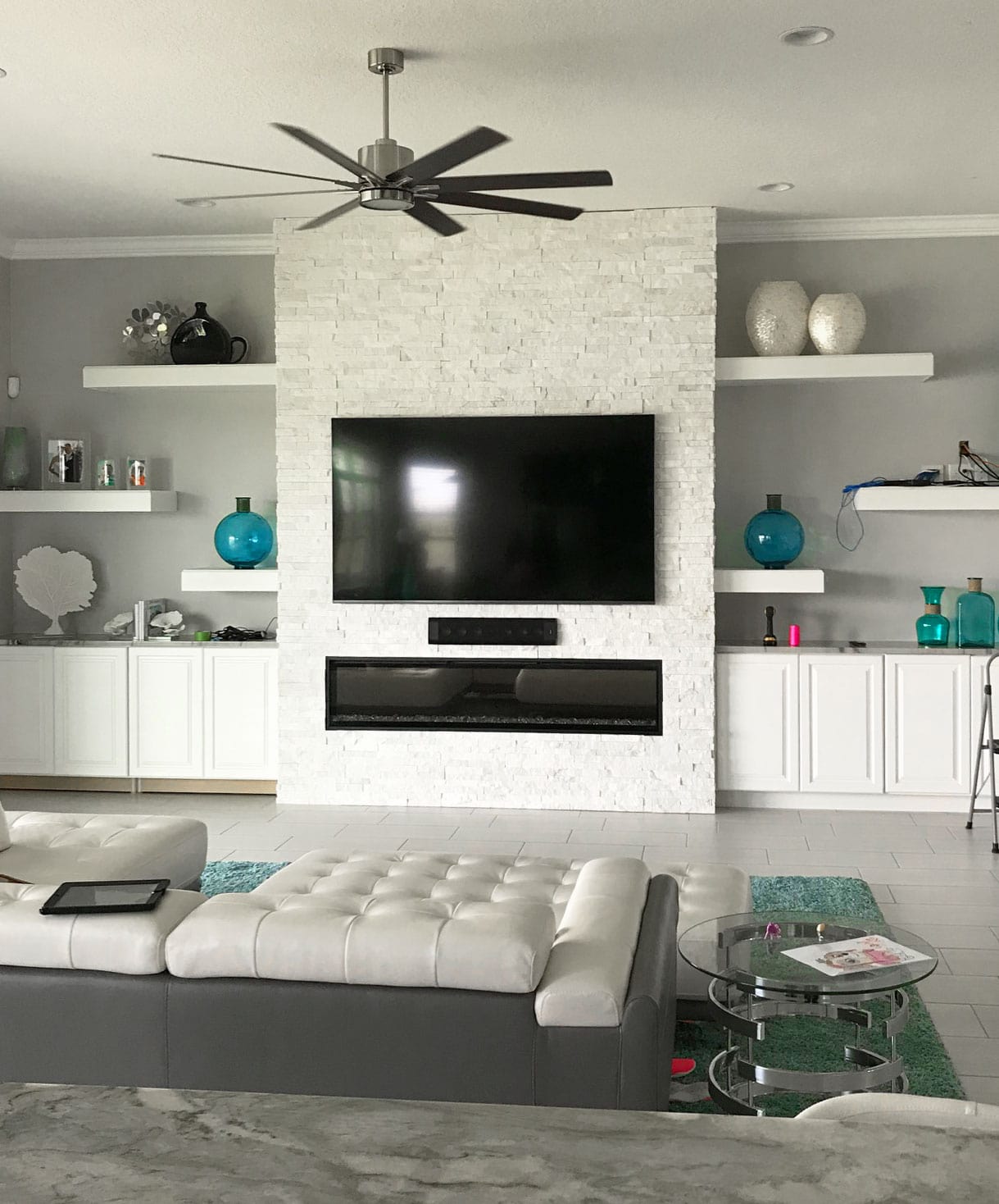 White Stacked Stone Fireplace with large tv and long linear fireplace flanked by built in cabinetry and floating shelves